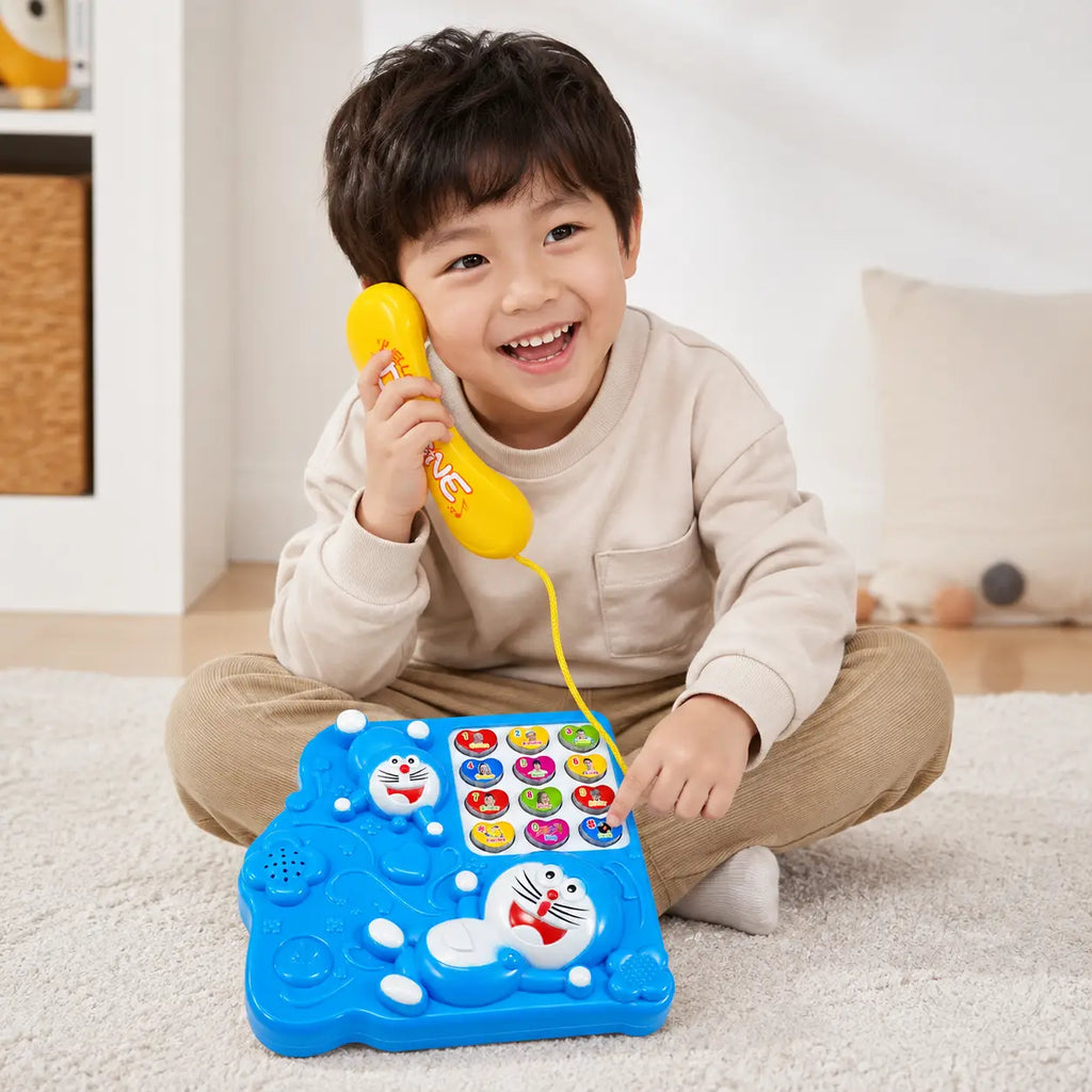 Young child playing with a blue Doraemon musical telephone toy and holding the yellow handset