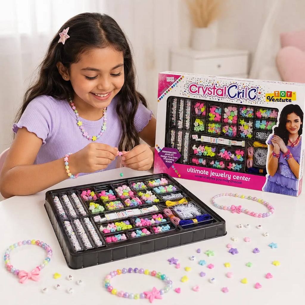 A young girl smiling while making colorful beaded jewelry with a Crystal Critic Ultimate Jewelry Center kit on a white table. The open black organizer tray is filled with multicolored beads and small accessories, with several finished pastel beaded bracelets and charms scattered around.